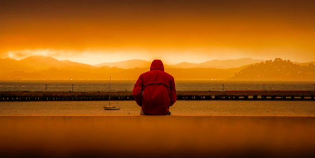 Senior Wearing Red Hoodie Sitting In Front of Body of Water, Corona Estate Planning Attorney.