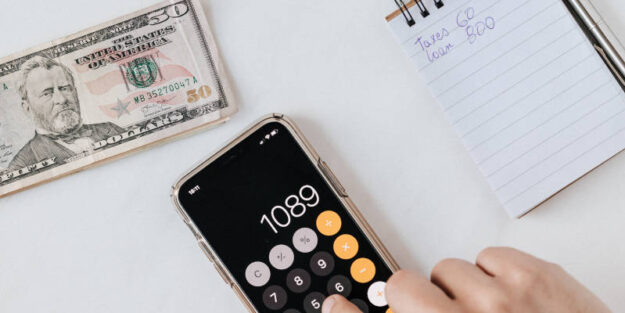 Anonymous Person Calculating Profit on Smartphone Calculator Near Banknotes and Money, Estate Planning Attorney.