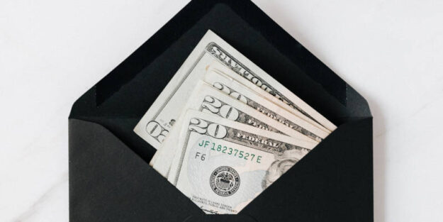 A Black Envelope With Cash Dollars on a Marble Table, Estate Planning Attorney.